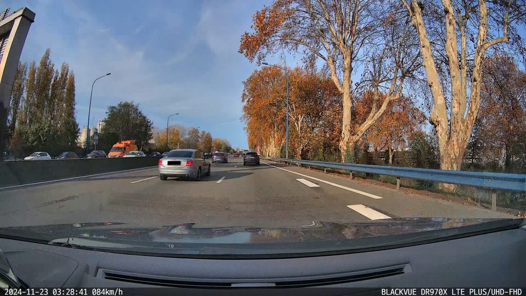 Capture d'écran d'une vidéo de dashcam montrant une route avec un arbre sur la droite et une voiture grise devant à gauche. L'horodatage en bas de l'image certifie l'heure et la date de l'événement.