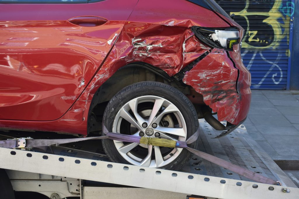 Voiture rouge accidentée avec aile arrière gauche endommagée et roue abîmée, correctement arrimée sur une dépanneuse. Illustration de l'utilité d'une dashcam pour documenter les accidents.